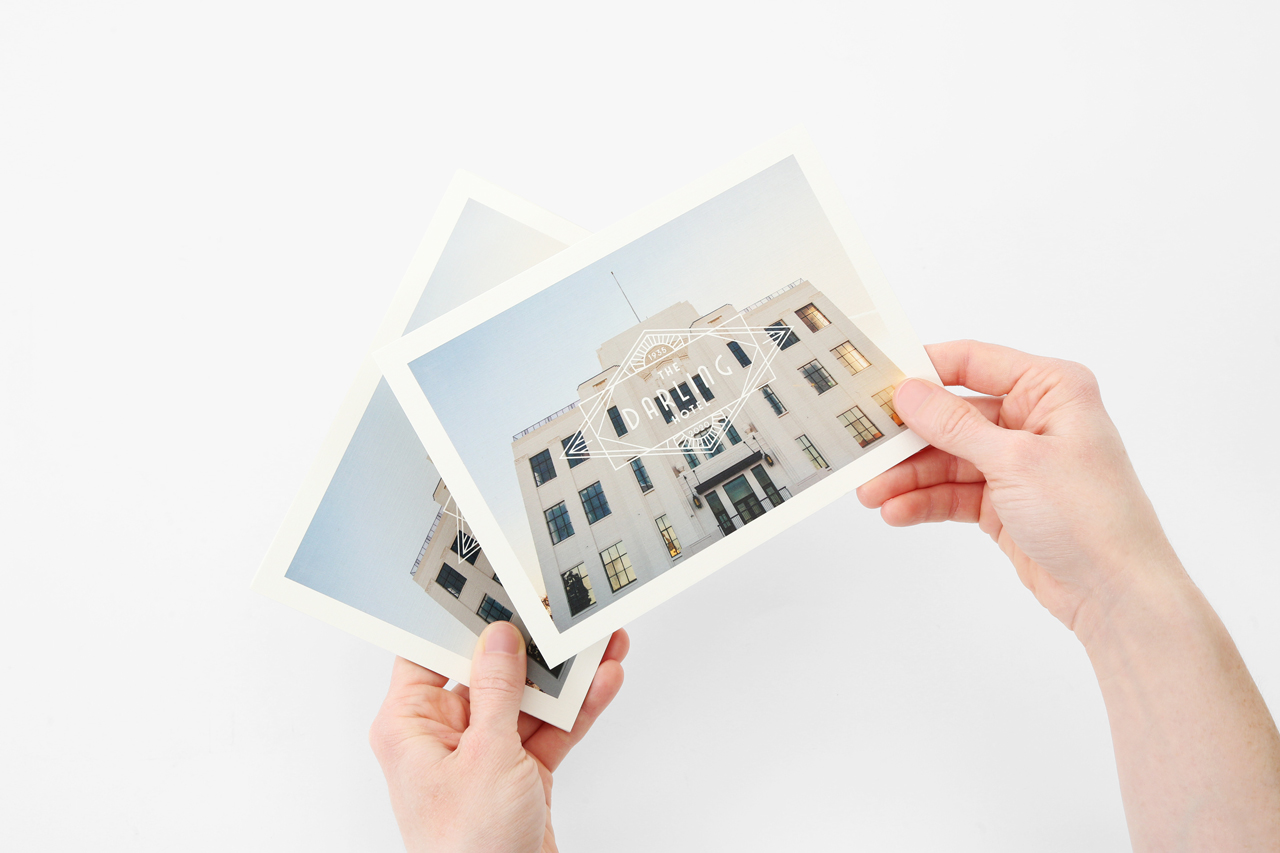 Two hands holding two postcards with an image of a hotel on them.