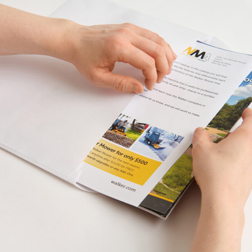 Two hands inserting a Walker Mower product catalog and letter into a white envelope.