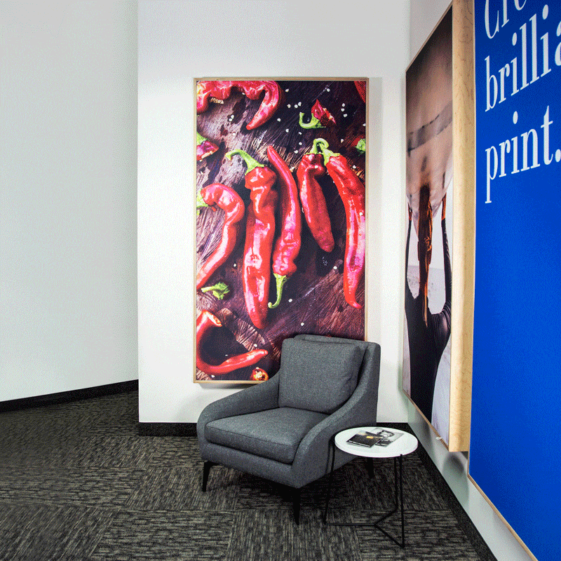 An office lobby with a gray chair, white side table and three SEGs handing on the walls.