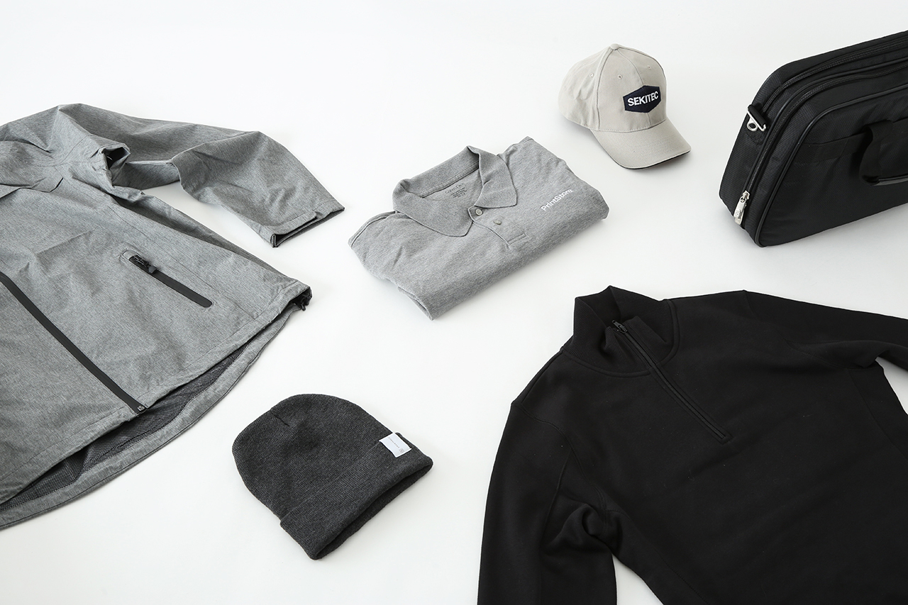 A collection of promotional products laid out, including a jacket, polo, hats and a laptop bag.