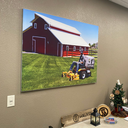 A picture of a man on a riding lawnmower in front of a big red barn hanging on a wall.