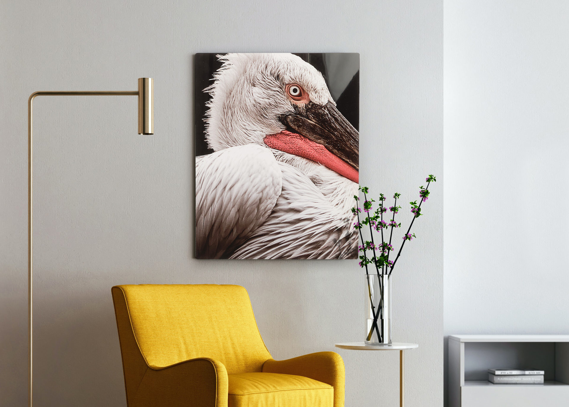 A custom metal print of a pelican hanging on a wall next to a yellow chair, side table and lamp.