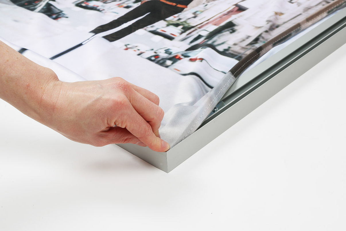 A hand inserting SEG fabric into its aluminum frame.