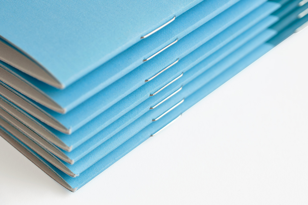 A stack of booklets with a saddle stitched binding and a light blue design.
