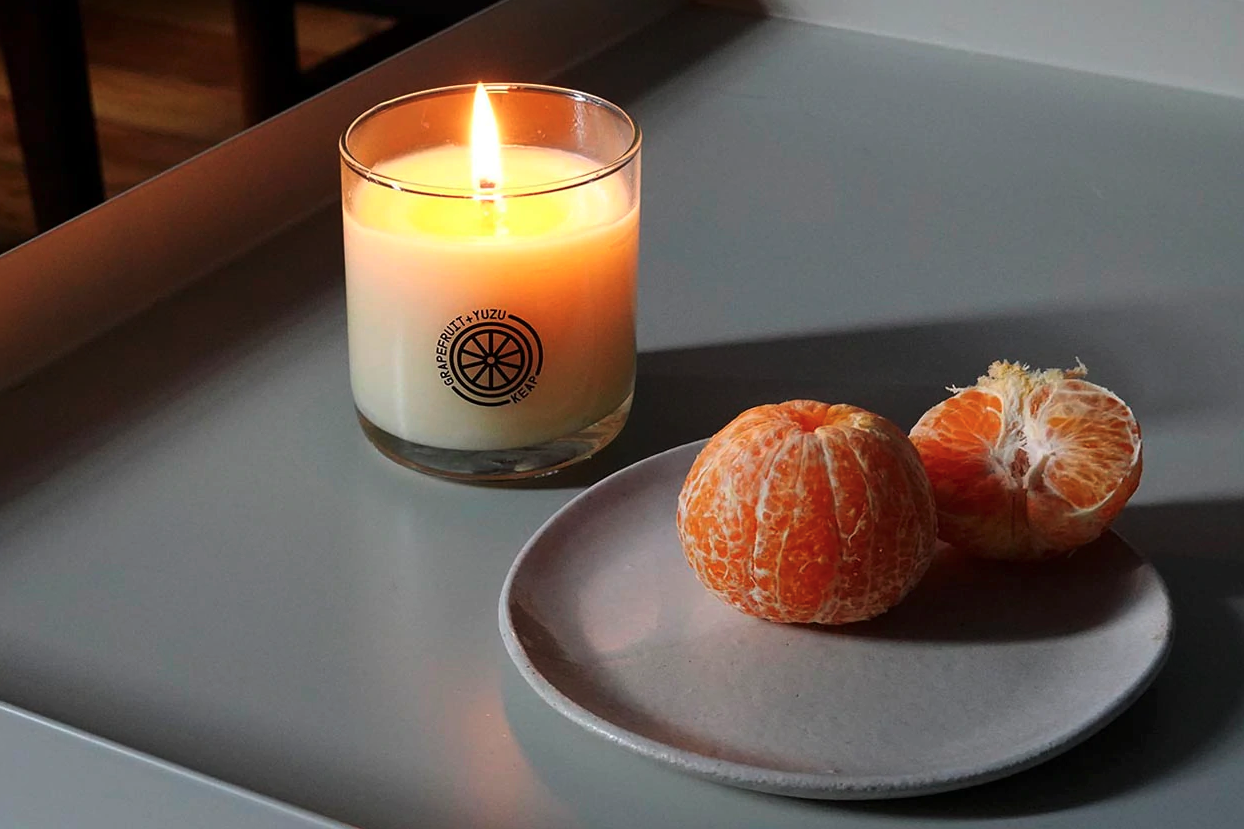 The Grapefruit+Yuzu candle from Keap next to a gray plate with two peeled clementines.