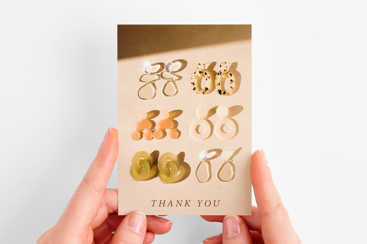 A custom postcard printed as a jewelry backer with six pairs of earrings attached to it.