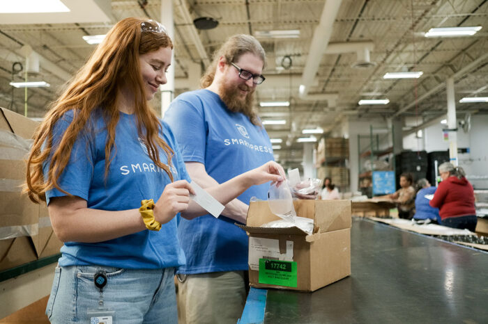 A man and a woman in Smartpress T-shirts sorting through materials in a box in a production area.