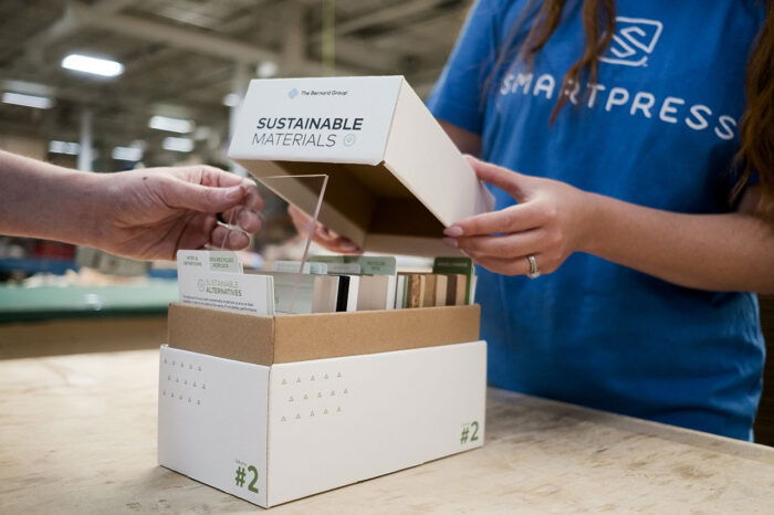 Two people standing at a table with a box of sustainable material samples in a production facility.