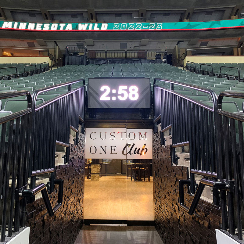 The entrance to the Custom One Club at the Xcel Energy Center with a large digital clock above the glass doors.