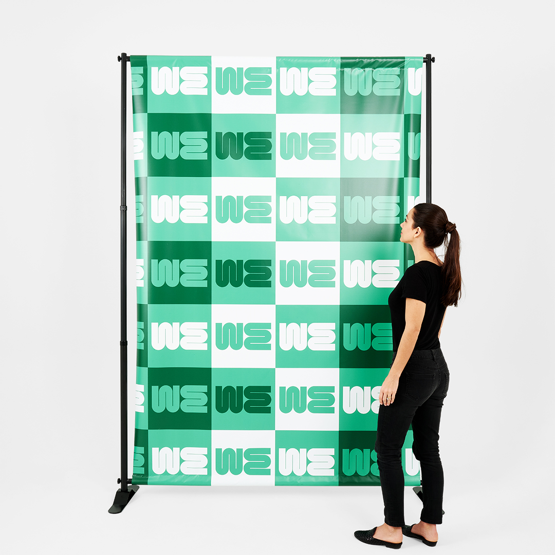 A woman wearing a black outfit standing next to a green and white step and repeat banner.