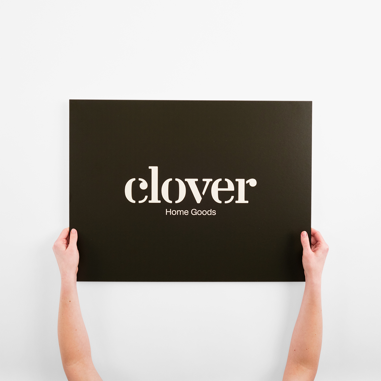 Two hands holding a custom eco-friendly sign printed with Clover Home Goods in white.