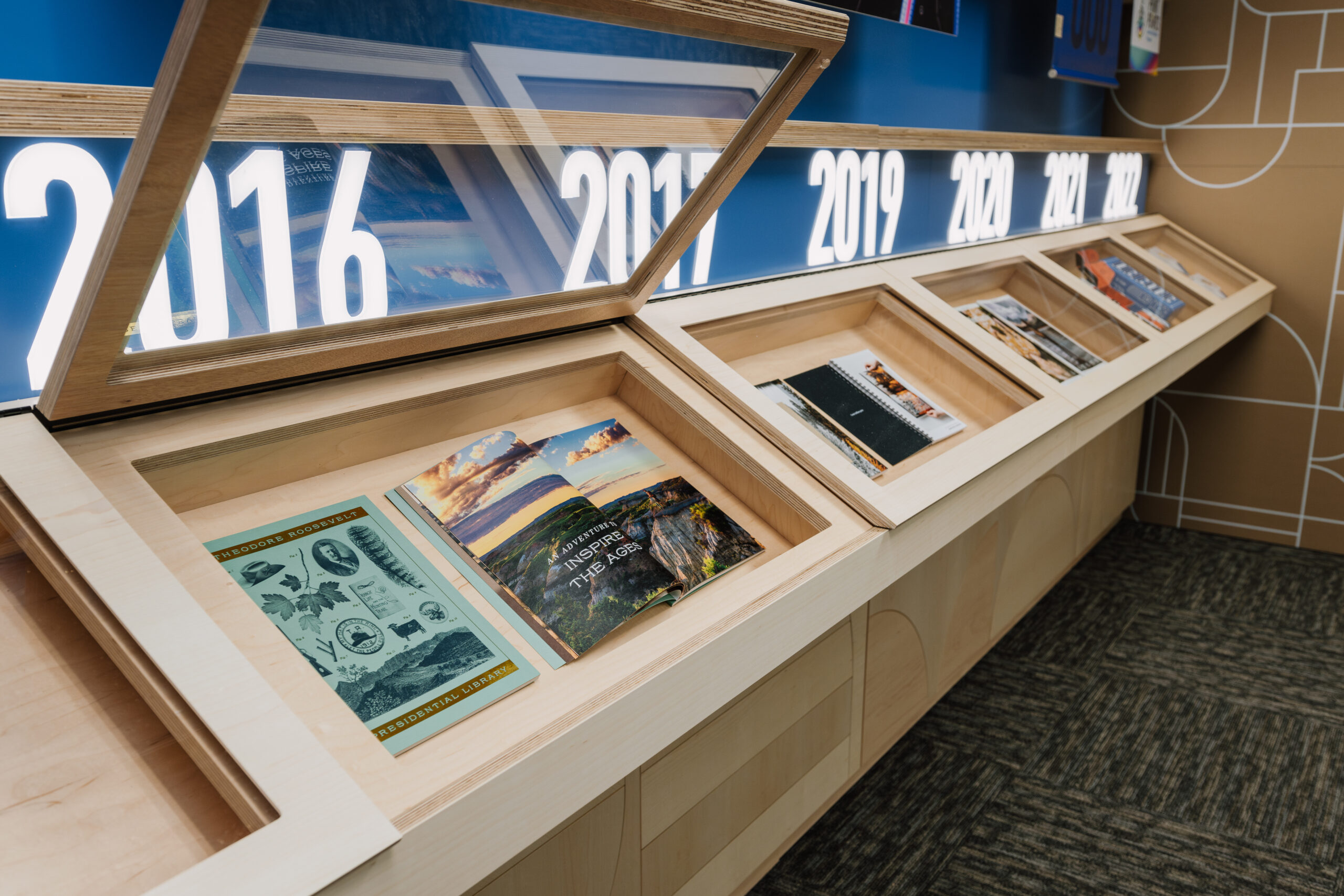 A custom wooden display case with shelves holding printed booklets underneath backlit dates.