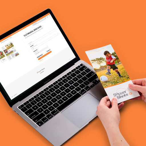 Two hands holding a vibrant Soccer Shots brochure, with a blurred background showing a laptop displaying their customized web-to-print software interface.
