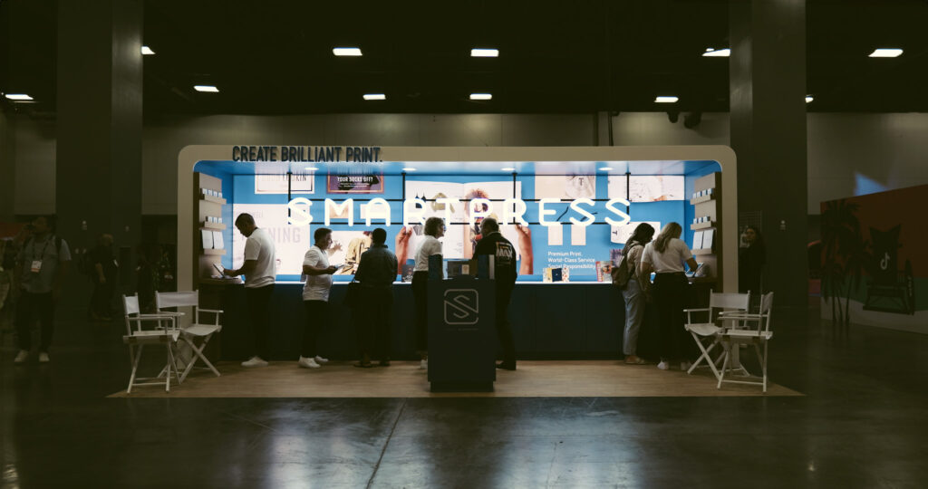 People conversing in front of the lluminated Smartpress booth.