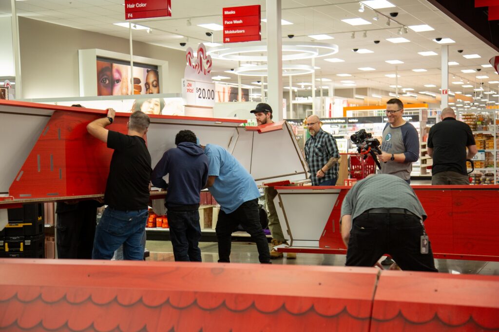A team of installation professionals working together to lift and assemble large structural roof components for an in-store holiday display.