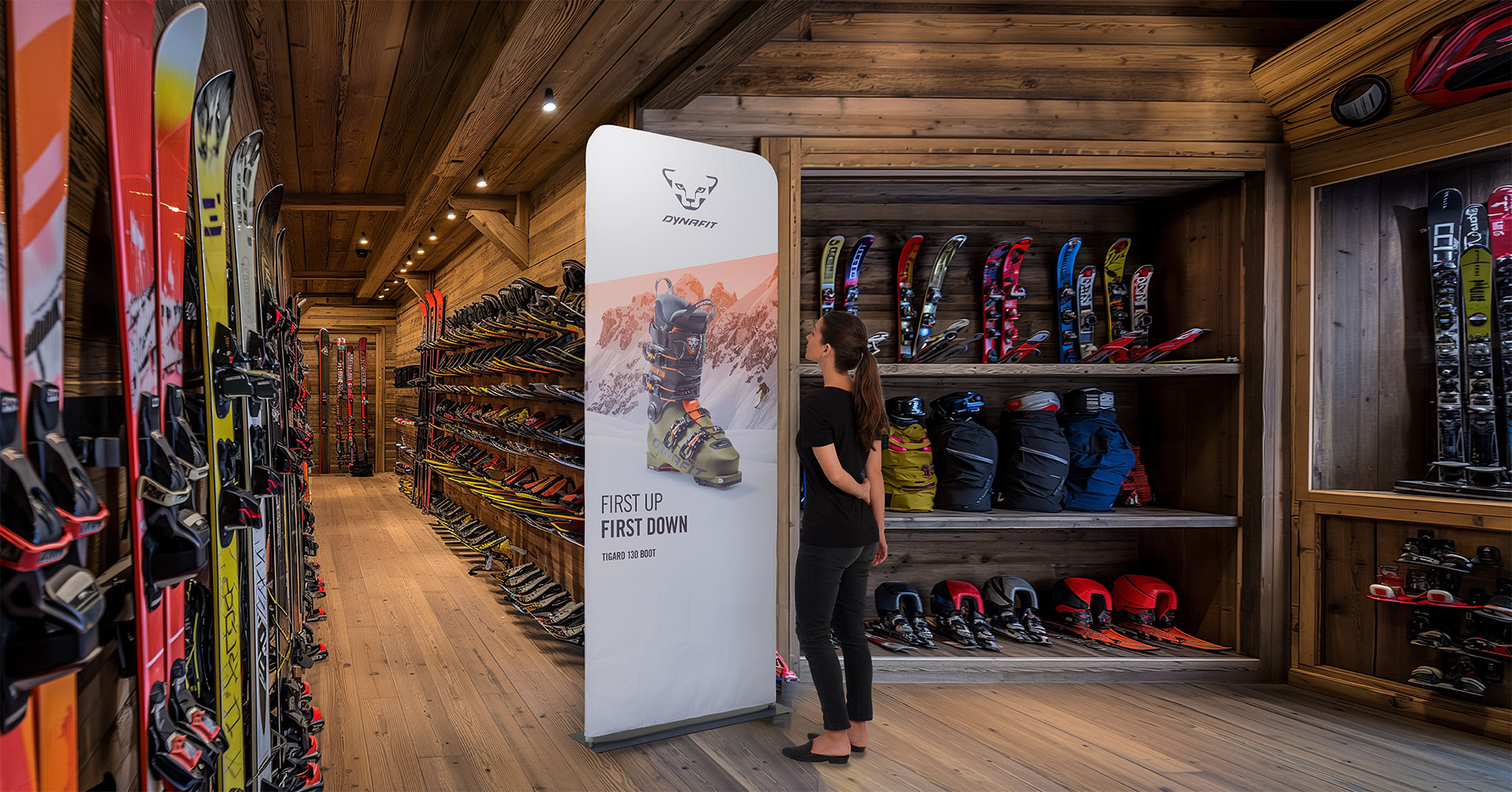 A woman standing by a tension fabric display printed with a snowboarding boot and mountain image.