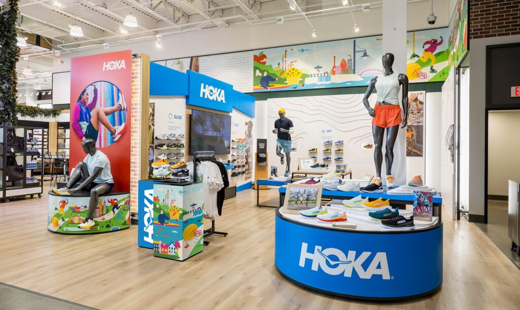 Vibrant HOKA retail setup featuring colorful graphic pillars, branded display tables, and athletic mannequins.
