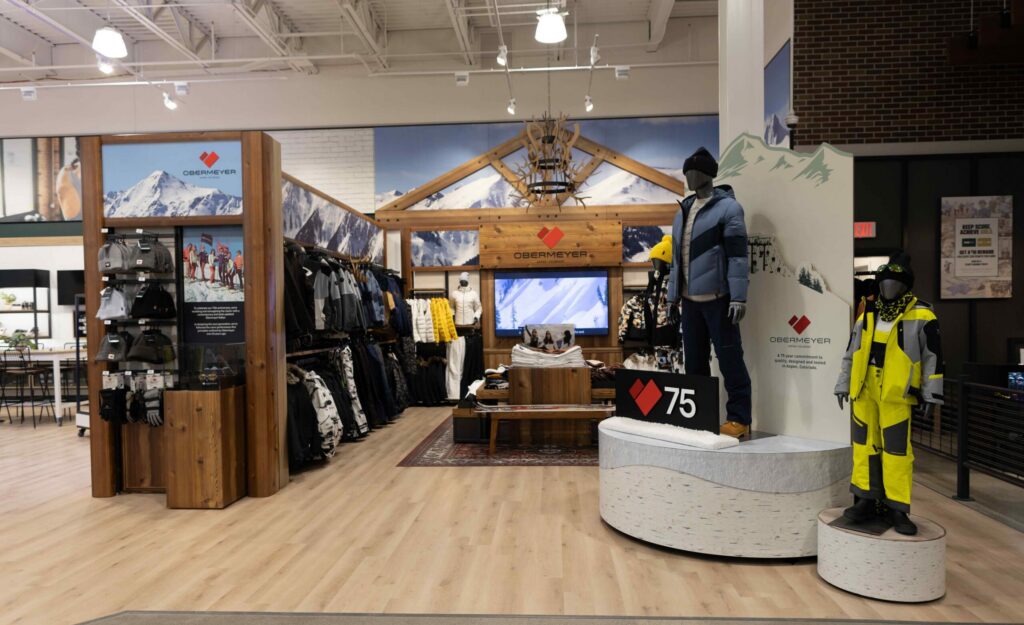 Obermeyer ski apparel retail environment featuring warm timber finishes, mountain graphics, and a 75th-anniversary milestone display.