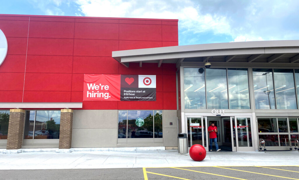 Large red "We're Hiring" outdoor banner mounted on the exterior brick facade of a Target store entrance.