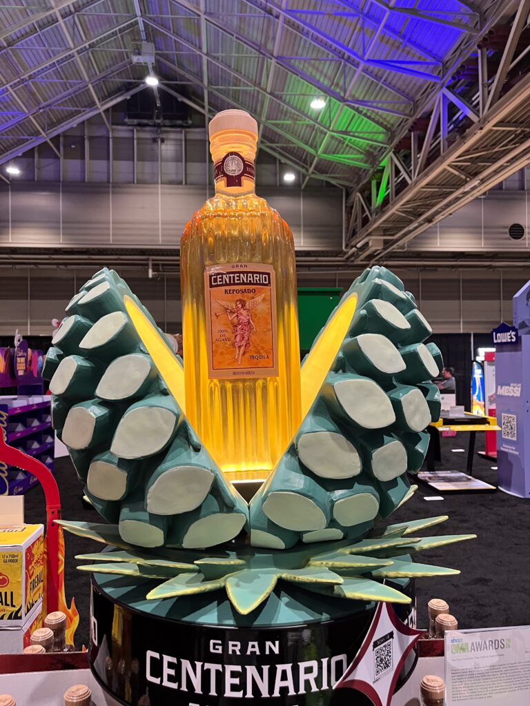 A sculpted resin blue agave piña display split open to reveal an illuminated 3D bottle replica of Gran Centenario tequila.
