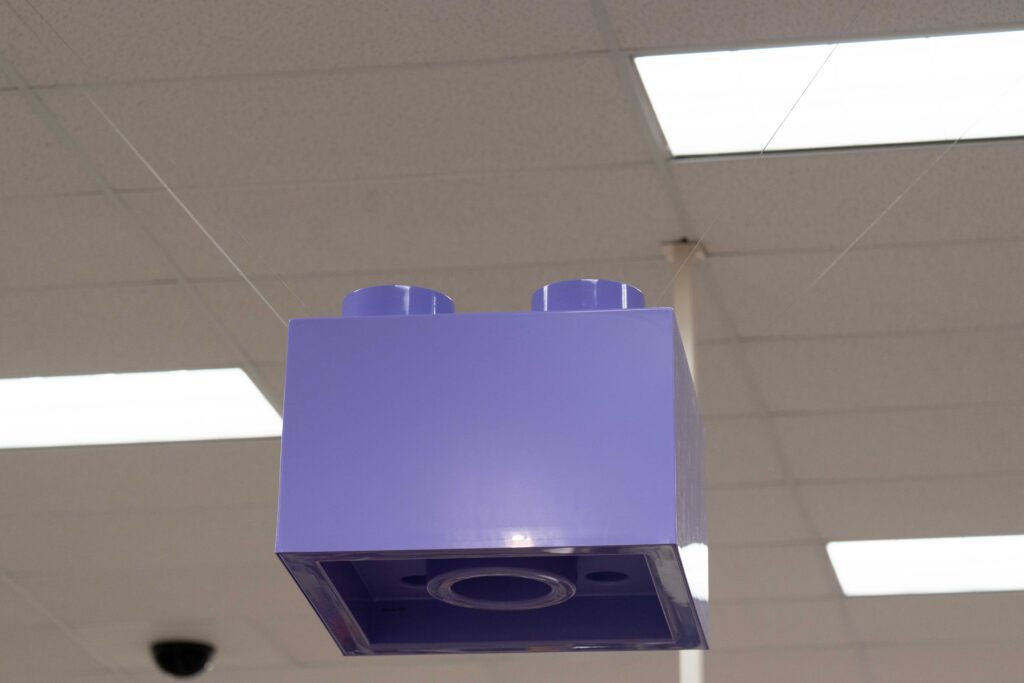 Close-up of a large purple LEGO brick fixture hanging directly below store ceiling light panels.