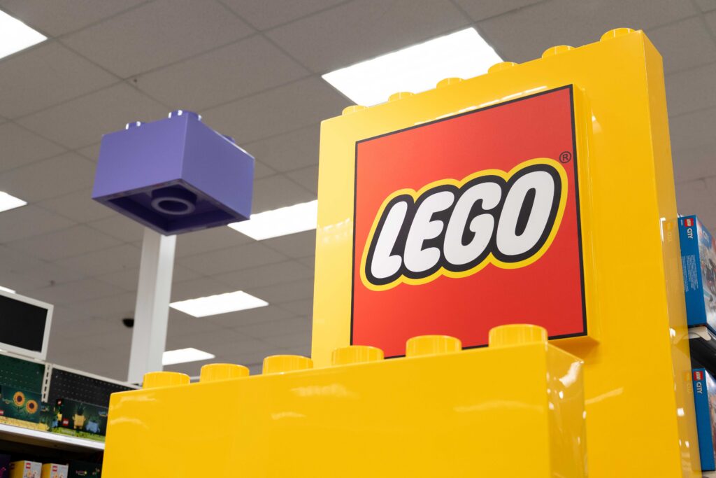Bright yellow signage tower with the red LEGO logo in front of oversized ceiling-suspended LEGO bricks.