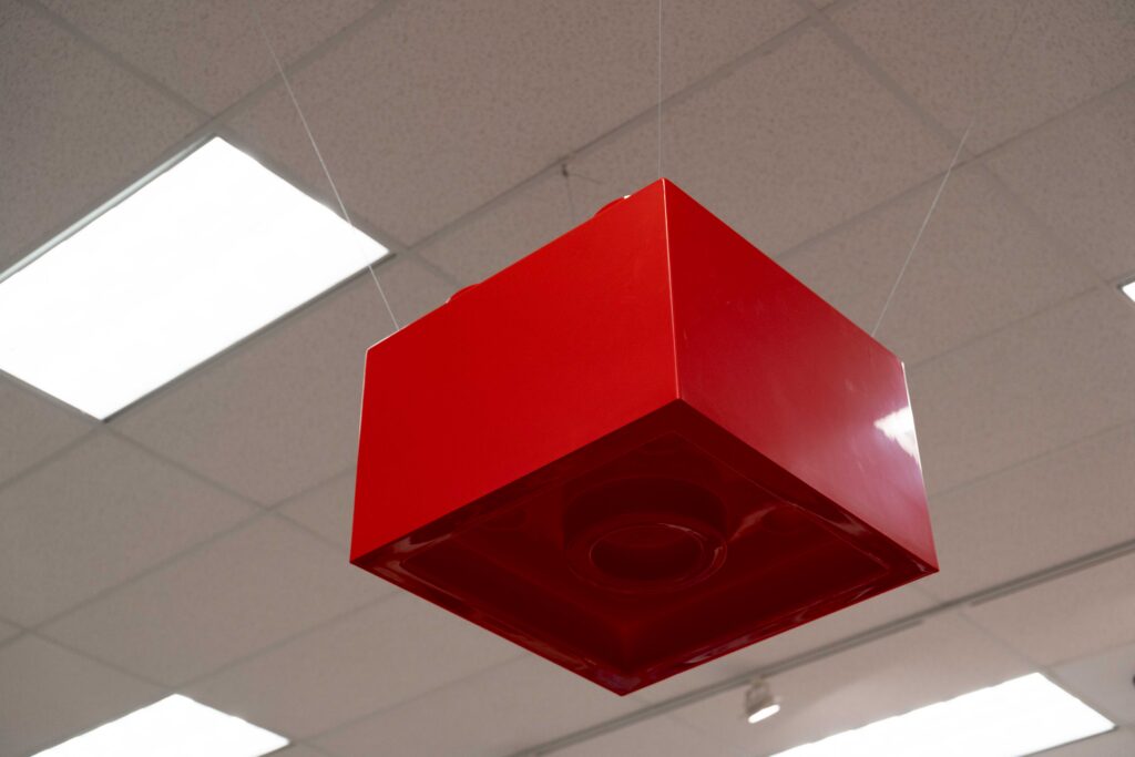 View looking up at an oversized red LEGO brick fixture attached securely to a store ceiling matrix.