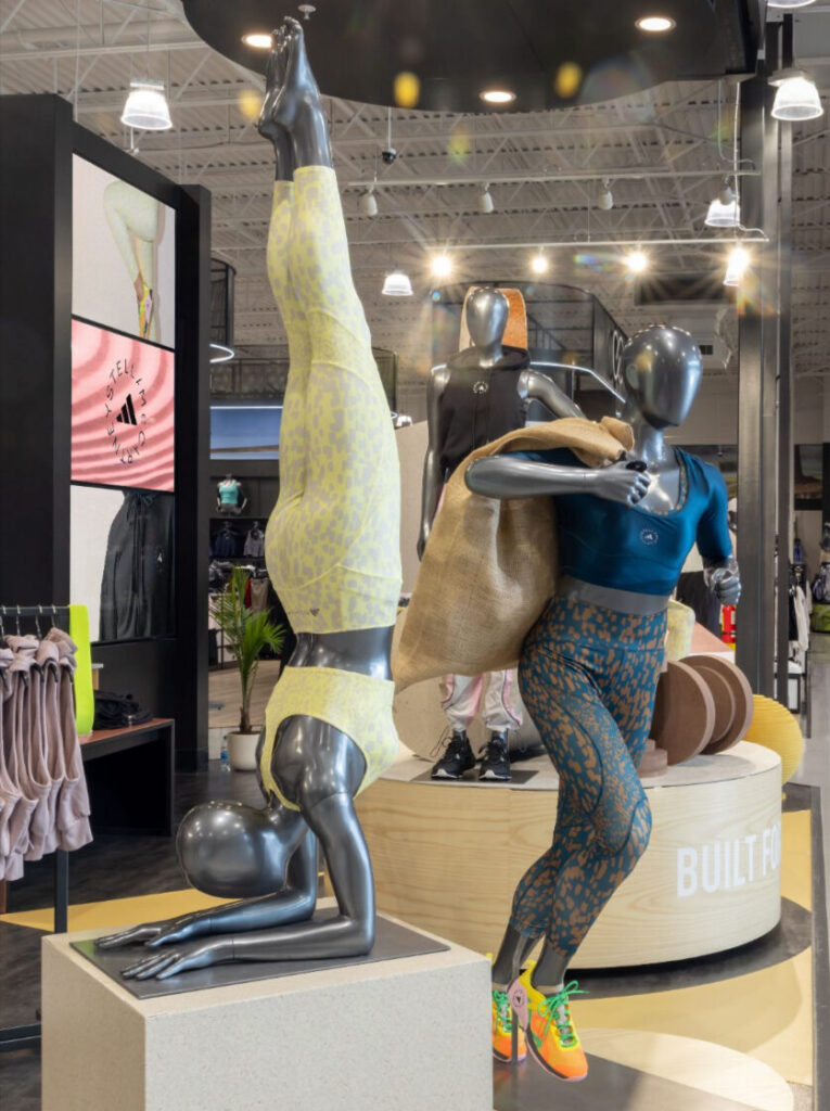 Dynamic athletic mannequins in active pose displays, including an inversion handstand, presenting activewear collections.