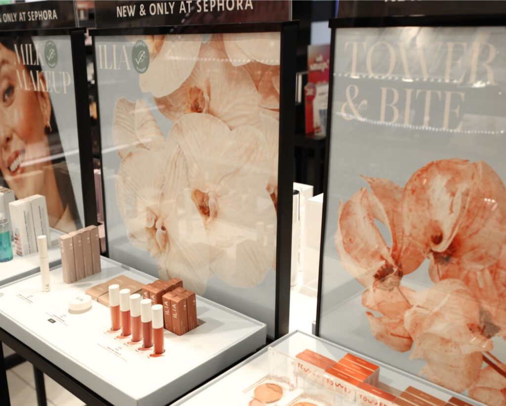 Sephora point-of-purchase counter display featuring floral backdrop imagery and lip products from Milk Makeup, Ilia, and Tower 28.
