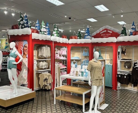 Snow-themed "Merry Cherry Chalet" holiday display at Target featuring festive paper-pulp tree structures, apparel racks, and styled mannequins.