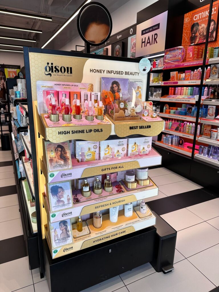 Multilevel Gisou retail display stand showcasing honey-infused beauty products with high-shine lip oil messaging in a store aisle.