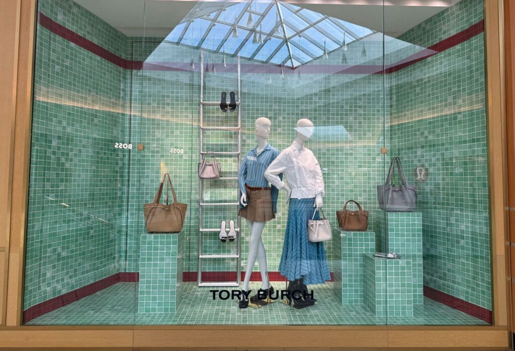 Tory Burch luxury window display featuring green tiled walls, skylight architecture, mannequins, and handbag pedestals.