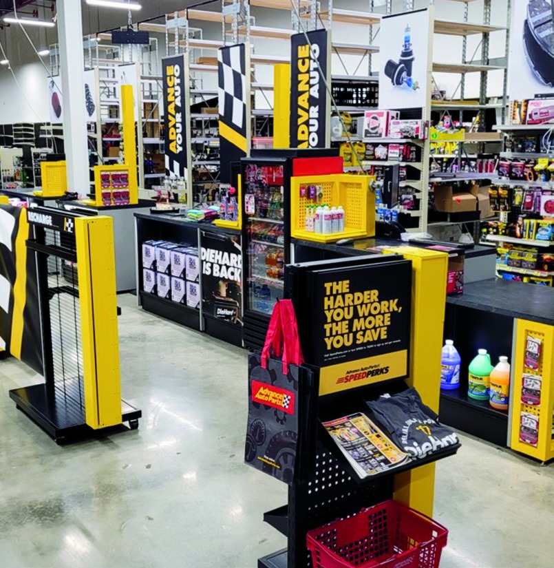 Point of Purchase floor display near an Advance Auto Parts checkout counter featuring impulse add-ons and promotional signage.