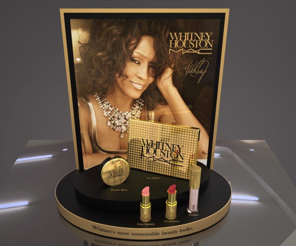 Elegant gold-accented MAC counter display featuring the Whitney Houston cosmetics collection and promotional portrait imagery.