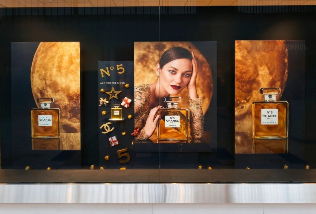 Chanel No. 5 storefront window display featuring large illuminated golden moon graphics, fragrance bottle imagery, and campaign posters.
