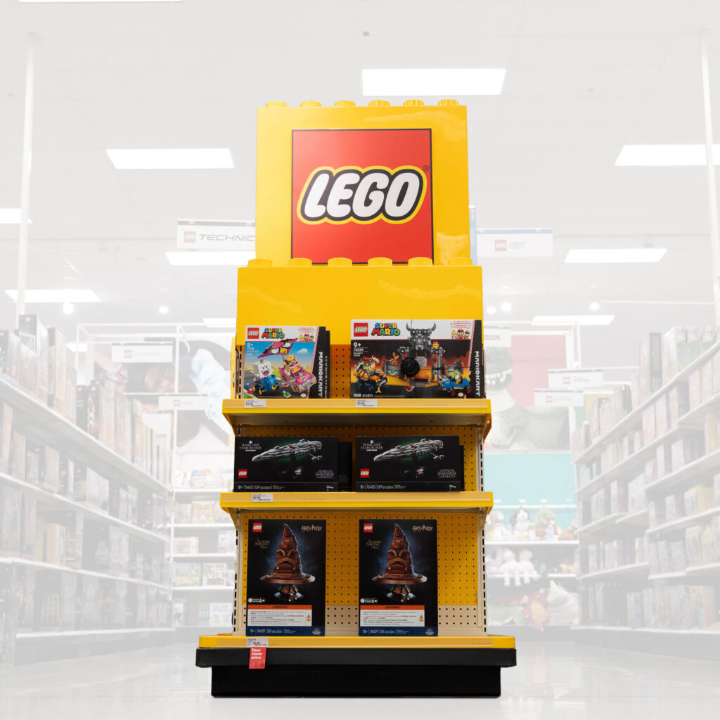 Endcap display featuring LEGO products, capped with a giant red LEGO logo display and oversized colorful LEGO bricks suspended from the store ceiling.
