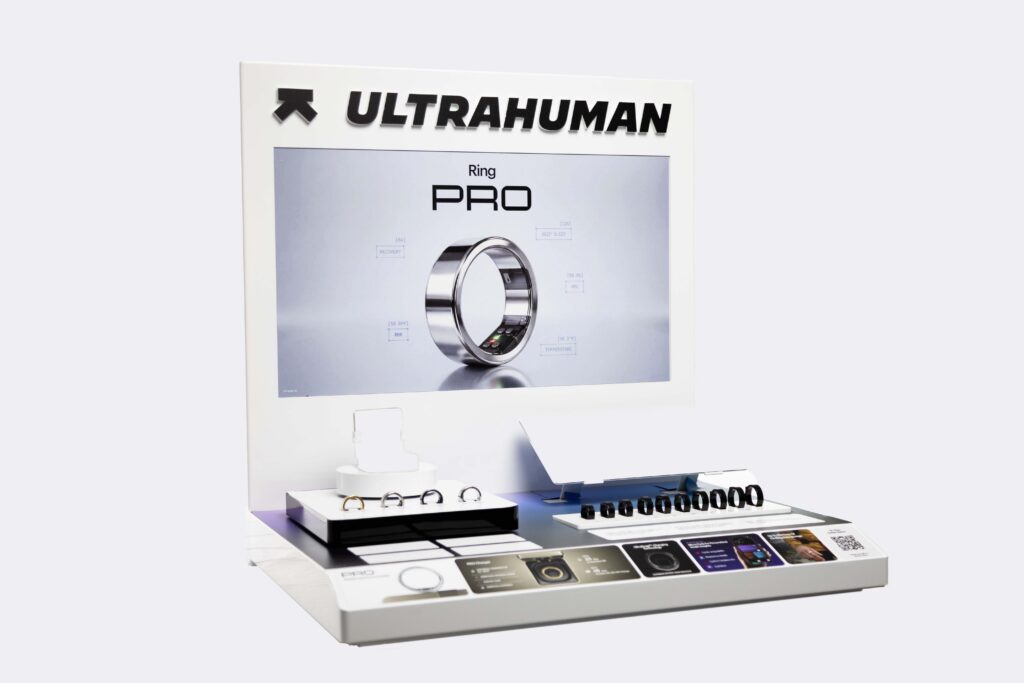 Isolated studio photo of the complete Ultrahuman Ring AIR interactive countertop display with backlighting screen and product trays.